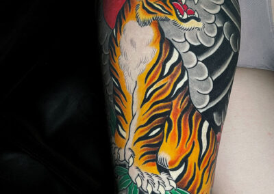 Japanese Traditional tattoo of full open mouth tiger standing rocks with red sun