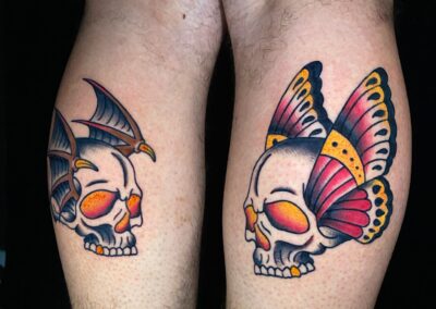 American traditional side by side skulls tattoos with wings in full color on back of legs