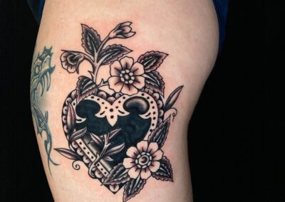 American Traditional tattoo of heart with flowers in black and gray